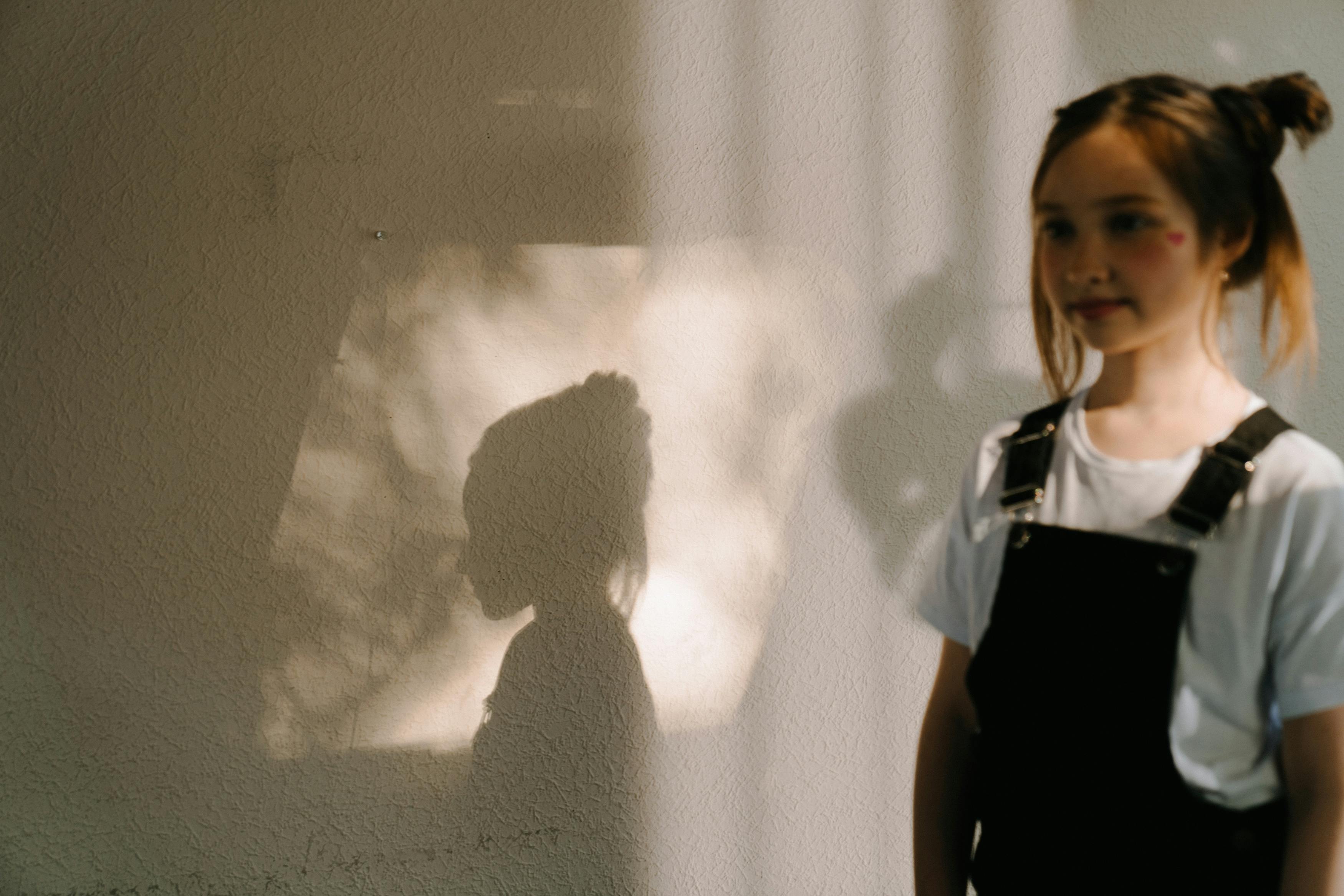 A young girl standing indoors, casting a playful shadow on the wall. Perfect for themes of youth and innocence.