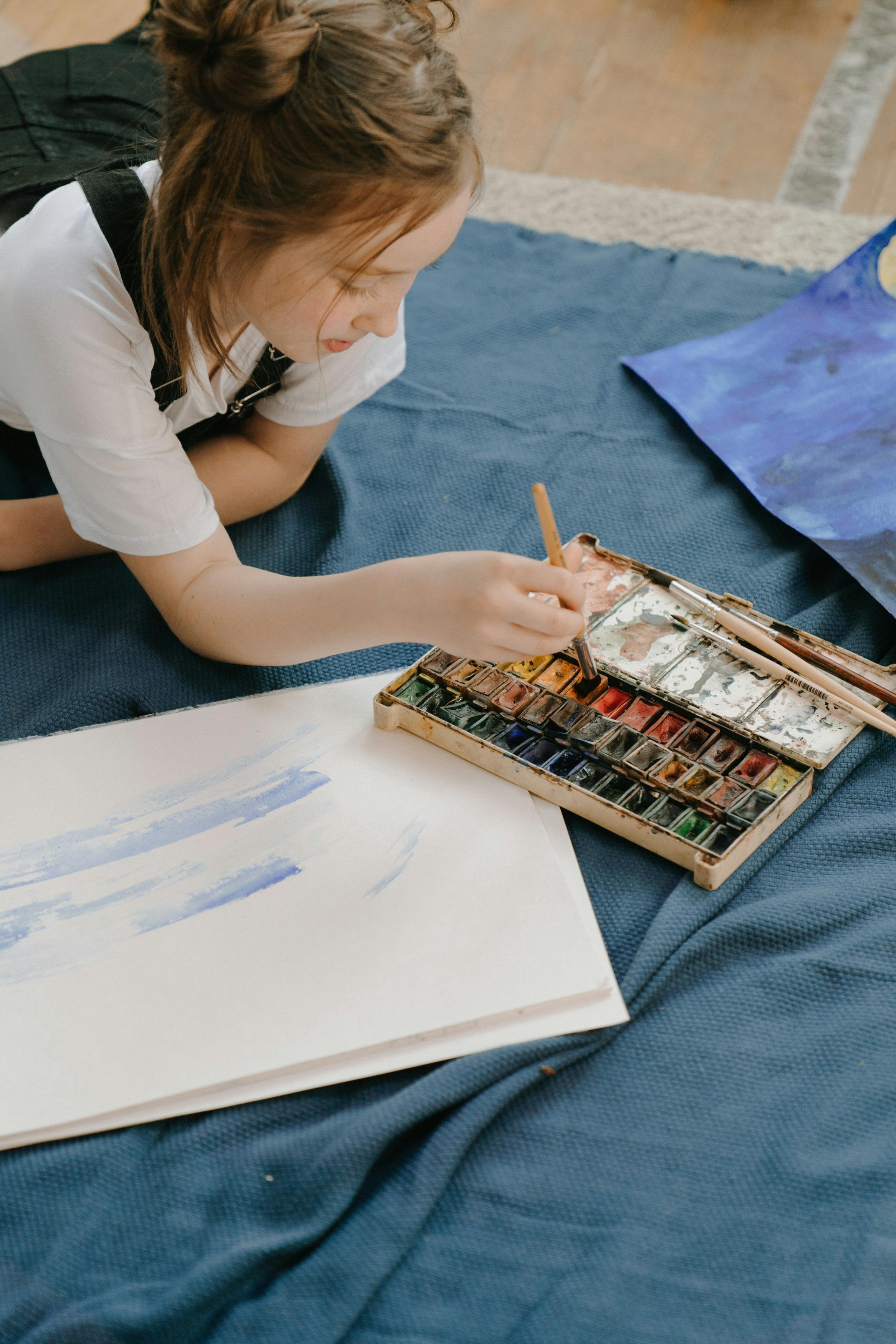 A young girl engaged in painting with a watercolor palette, enjoying a quiet indoor creative activity.