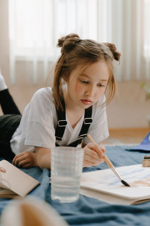 Free A young girl painting indoors, depicting the essence of creativity and leisure. Stock Photo