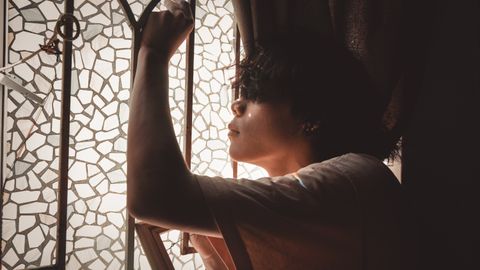 Side view of a young man posing thoughtfully by a mosaic glass window with soft light.