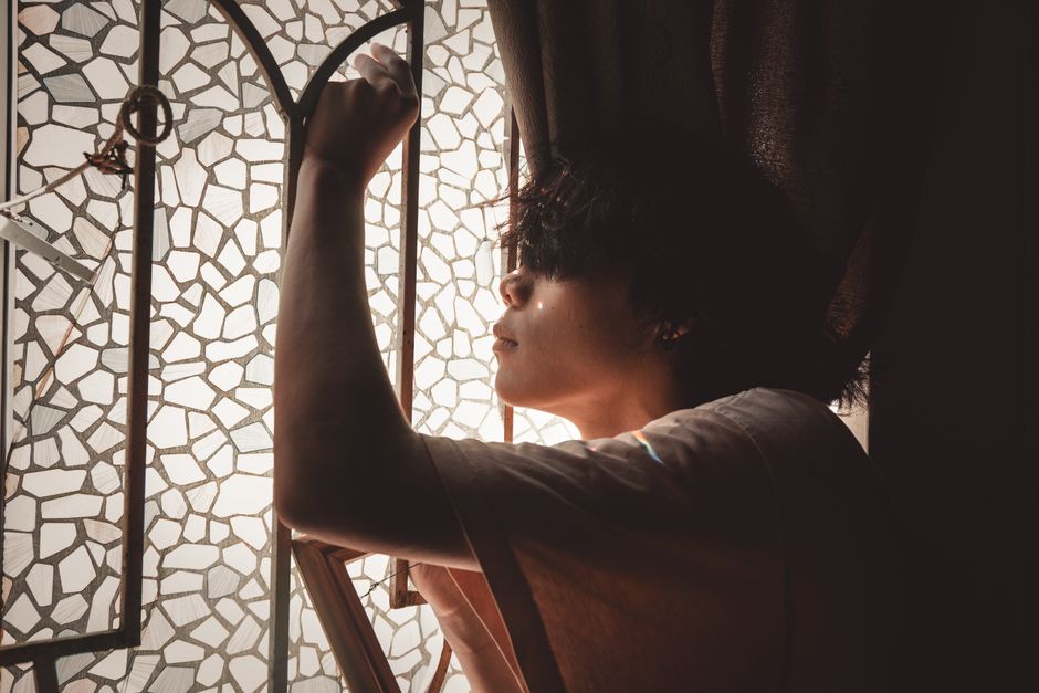 Person sitting pensively by a mosaic glass window — the careful consideration required before pursuing ibogaine treatment in Mexico or Canada for serious conditions