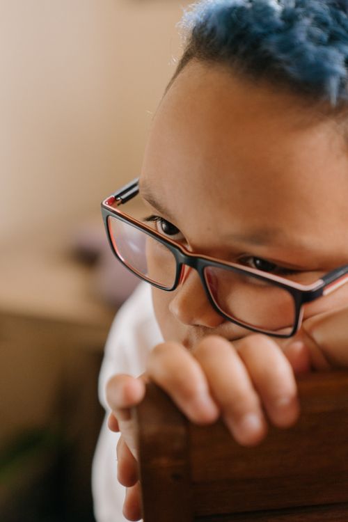 Free Close-up portrait of a child with blue hair and glasses, deep in thought indoors. Stock Photo