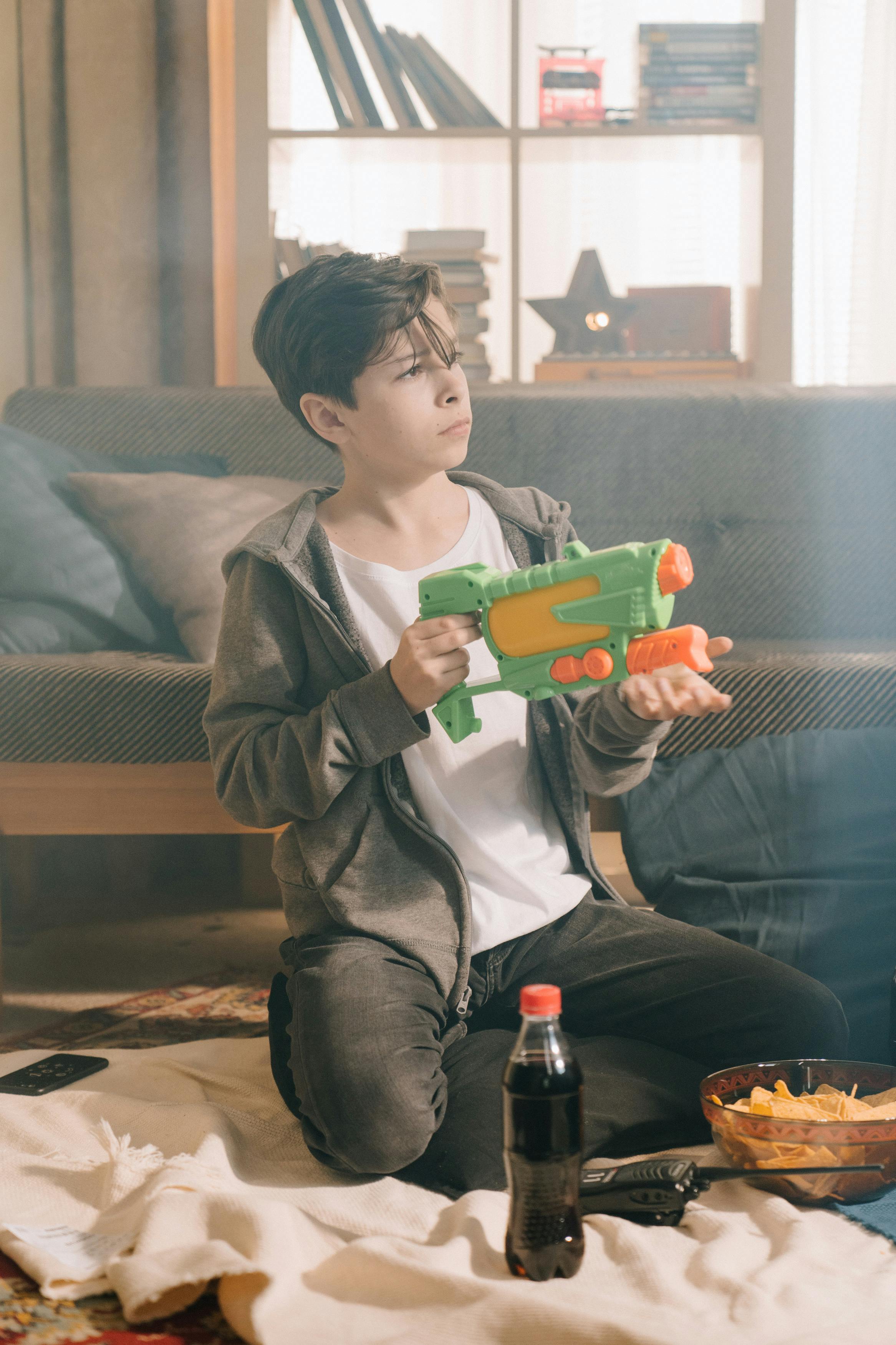 boy in black leather jacket holding green plastic toy gun