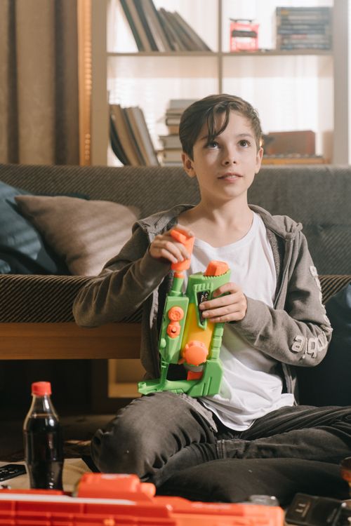 Free Young boy sitting indoors playing with a colorful toy water gun during leisure time. Stock Photo