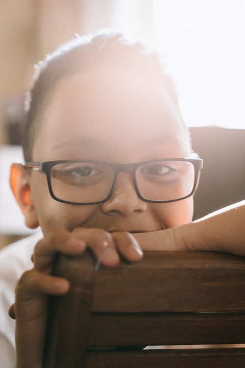Free A cheerful young boy with glasses smiles warmly in natural sunlight. Stock Photo