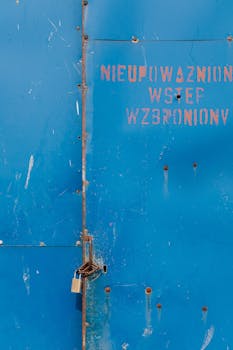 特写镜头对准一扇生锈的挂锁大门，门上带有波兰标志，警告禁止未经授权进入