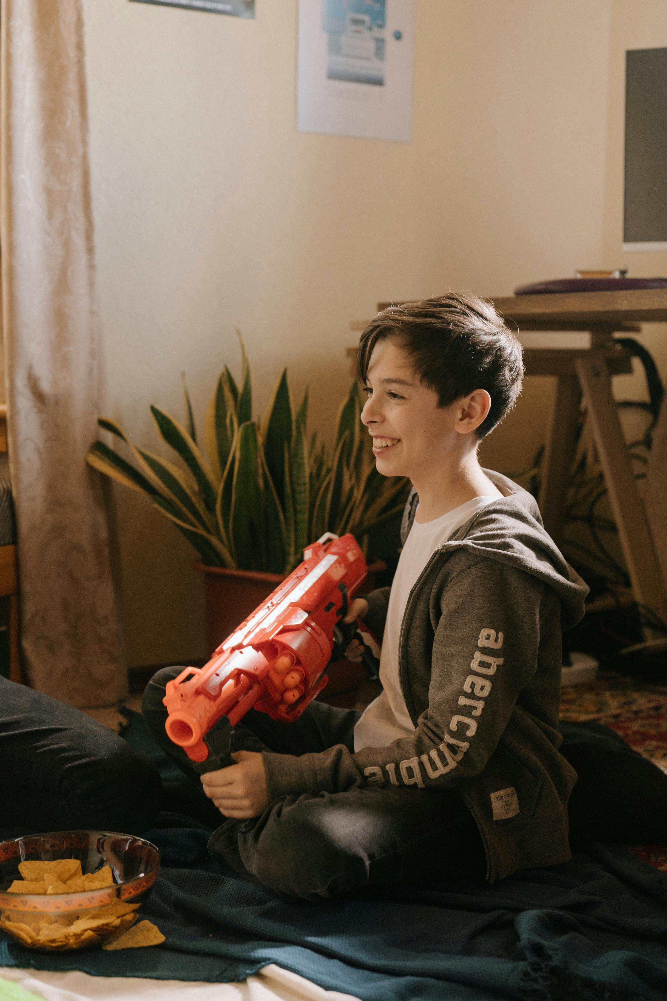 boy in black and gray jacket holding red plastic toy gun