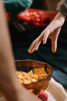 A close-up shot of a hand reaching for a bowl of corn chips, conveying a sense of hunger.