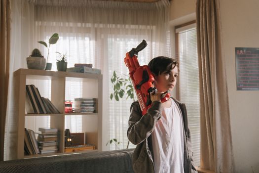 A young boy enjoys playing with a toy water gun in a cozy, well-lit living room setting.