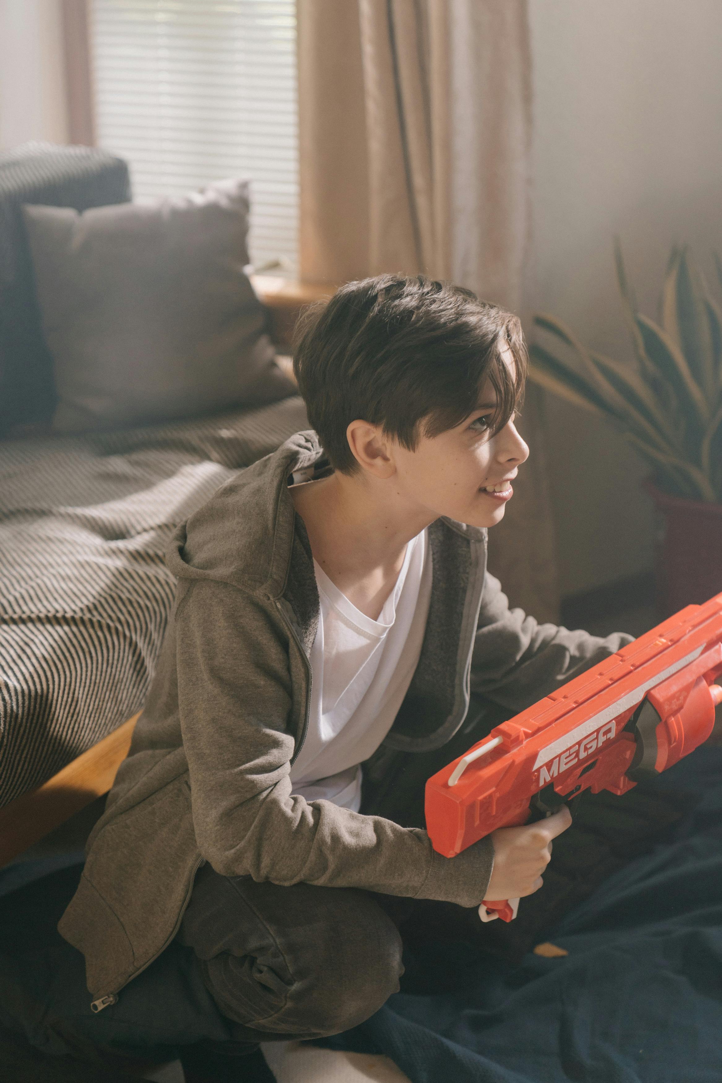 boy in gray hoodie playing red toy gun