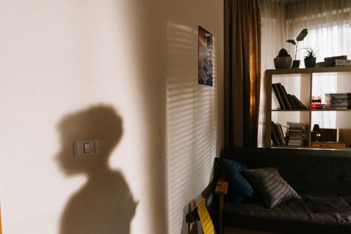Free A child's shadow cast on the wall in a cozy, well-lit apartment room with a bookshelf. Stock Photo