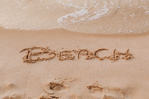 'Beach' written in sand as ocean waves gently touch it, creating a vacation vibe.