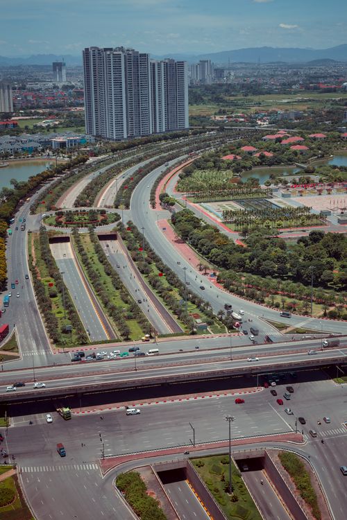 Free From above of cars driving on asphalt road near green bushes and modern buildings in sunlight in summer day outside Stock Photo