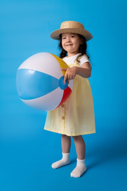 Free Girl in Brown Dress Holding White Blue and Yellow Inflatable Ball Stock Photo