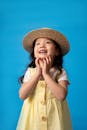 一位戴着草帽的迷人女孩，在充满活力的蓝色背景映衬下，展露着喜悦之情