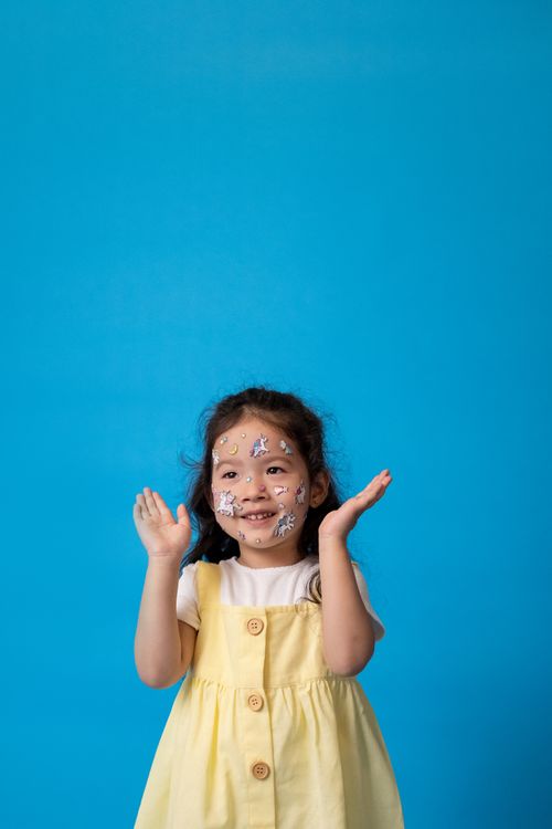 Free A happy child with unicorn face stickers against a blue backdrop. Stock Photo