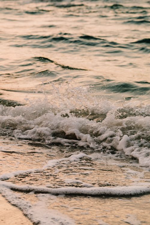 Free Peaceful ocean waves crash gently on the sandy shore during a beautiful sunset. Stock Photo