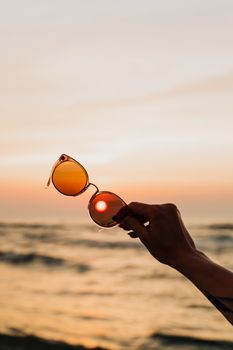 手持太阳镜，映衬着海边美丽的日落，捕捉宁静的海景