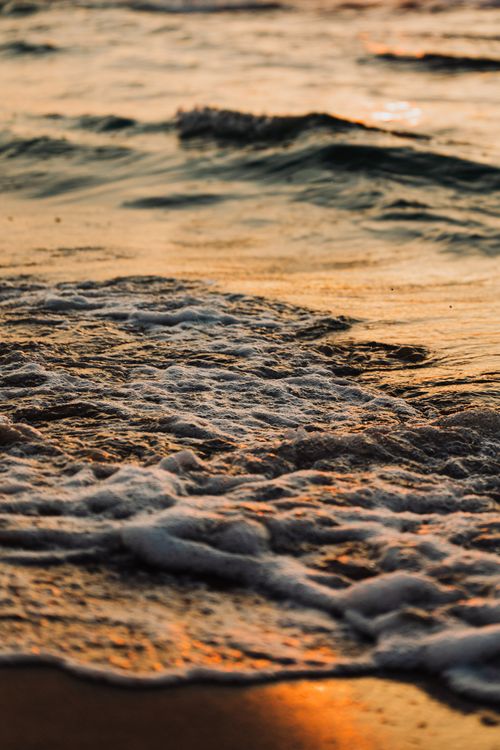 Free Serene ocean waves gently break on the sandy shore under a golden sunset sky. Stock Photo