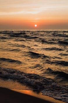 A stunning sunset over the ocean waves, blending warm colors with a serene beach atmosphere.