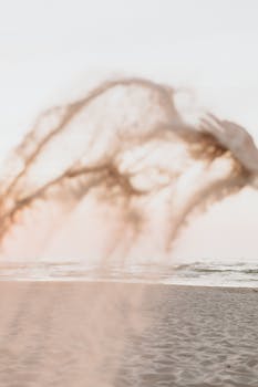 Blurred motion of sand tossed in the air with ocean waves in the background on a serene beach.