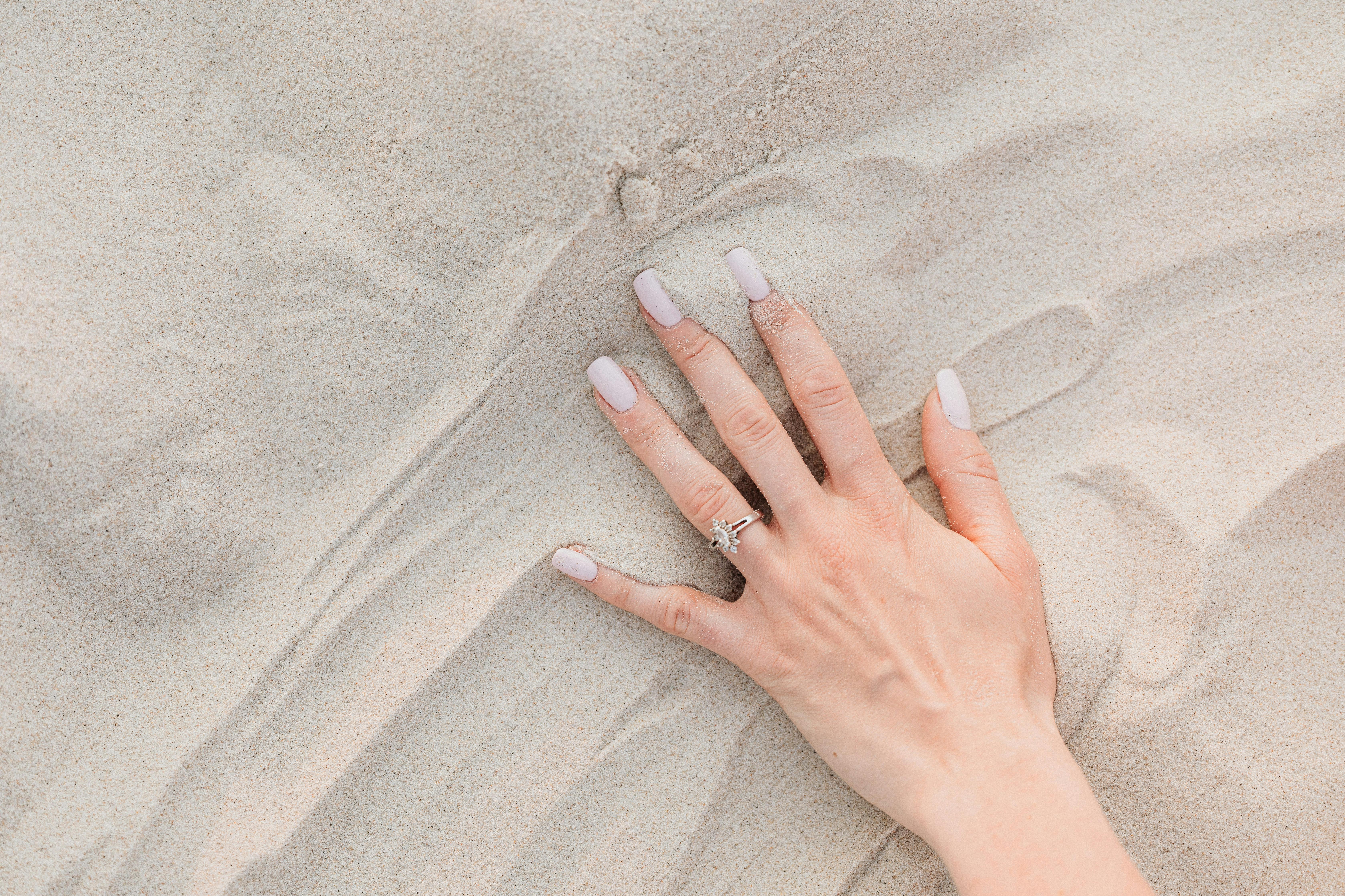 hands of a person wearing silver ring on white sand