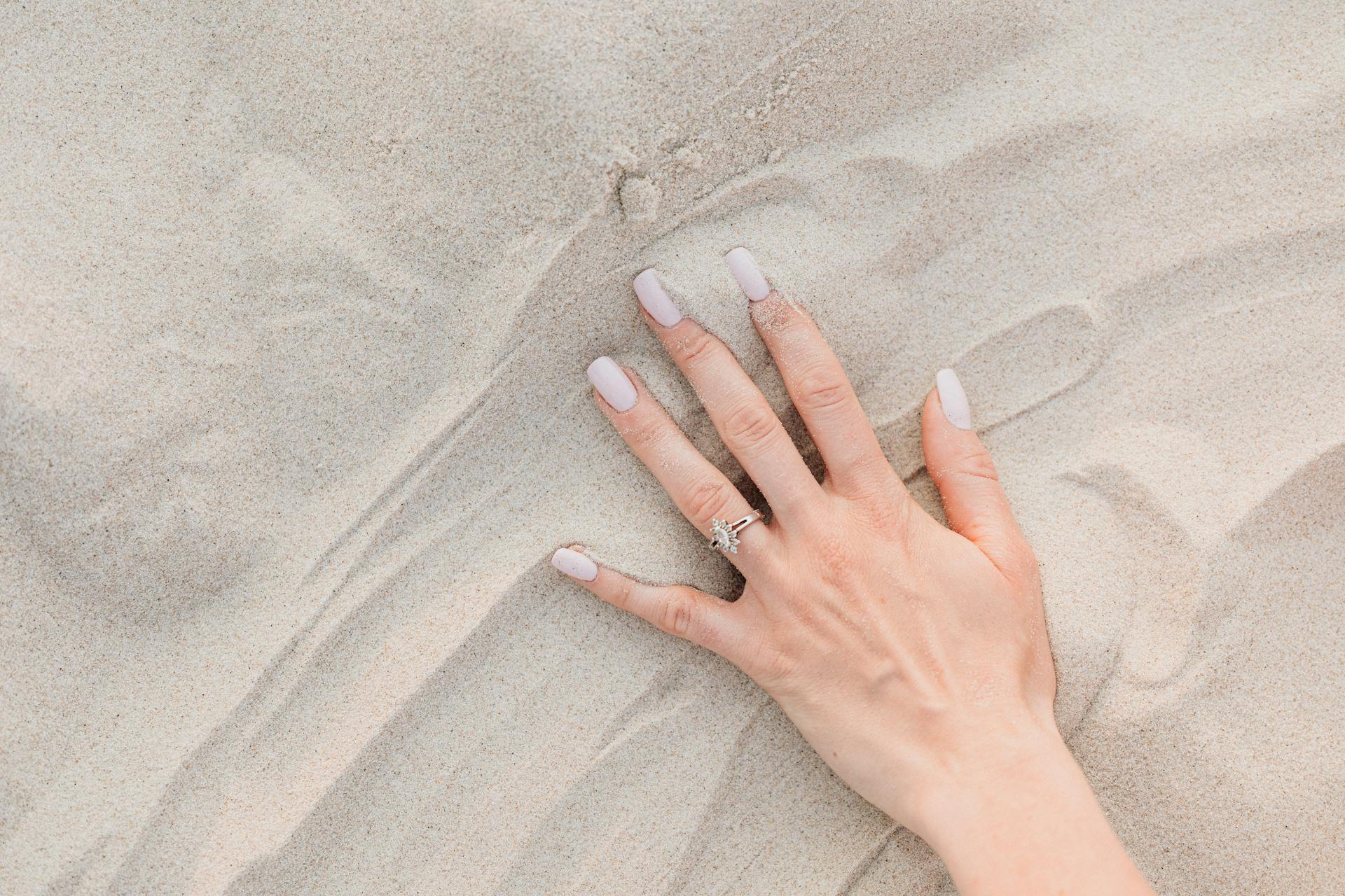 Hands of a Person Wearing Silver Ring on White Sand