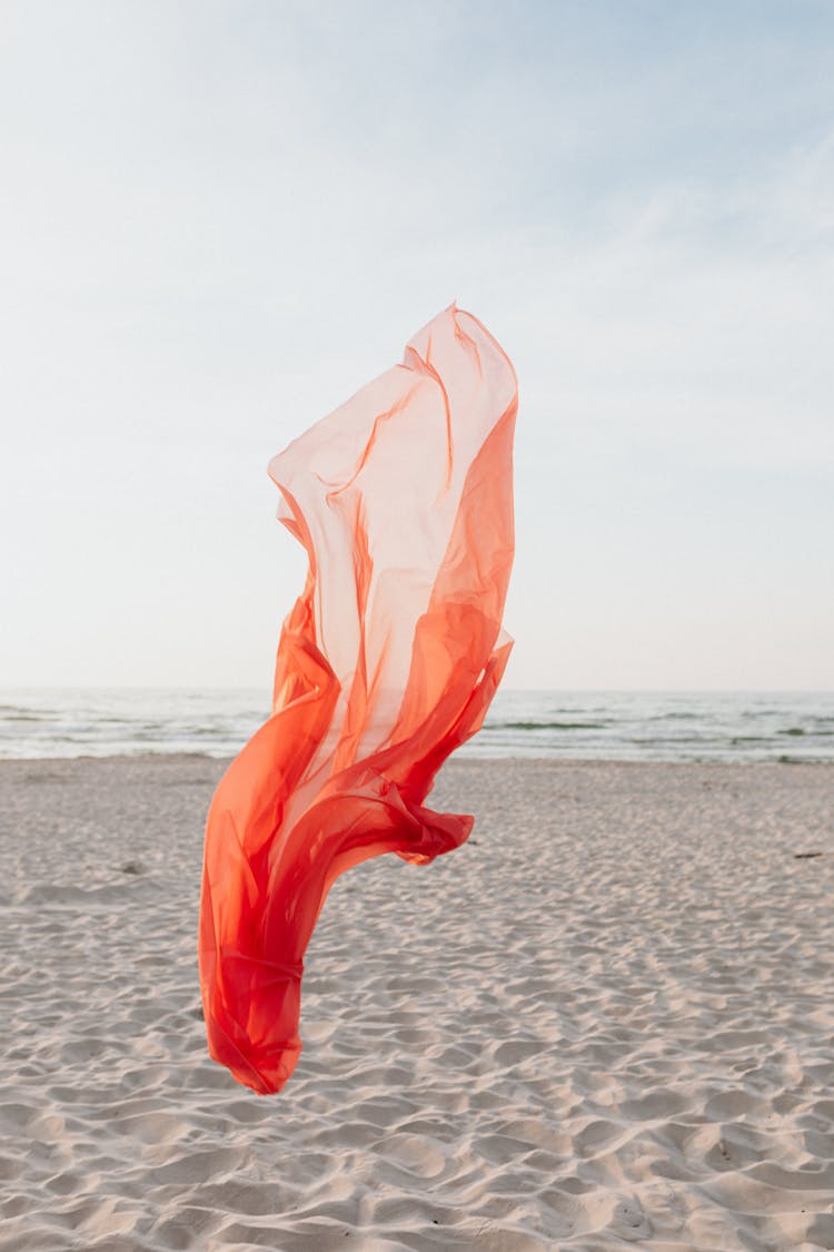 Wind Blowing On Orange Sheer Textile On Beach