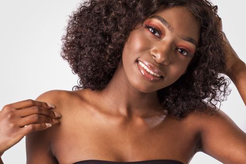 Free Close-up portrait of a smiling woman with curly hair and bare shoulders, exuding elegance and charm. Stock Photo