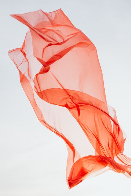 Vibrant red fabric gracefully flowing in the clear sky, capturing the essence of movement and lightness.