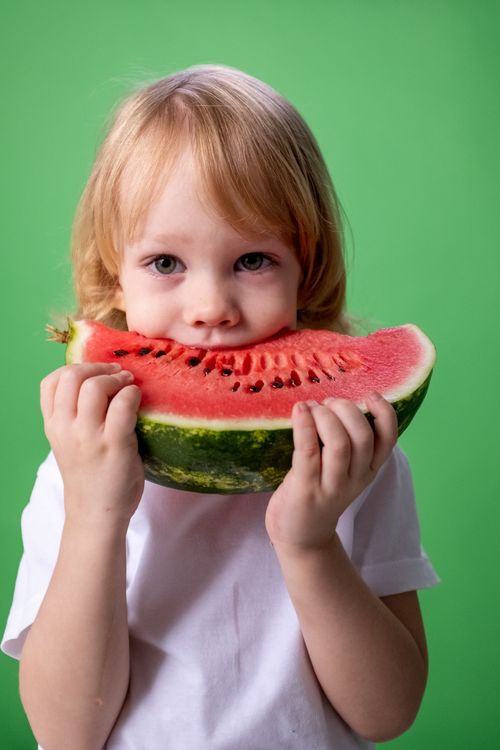 Free Cute child enjoying a fresh watermelon slice in a studio setting with a green background. Stock Photo