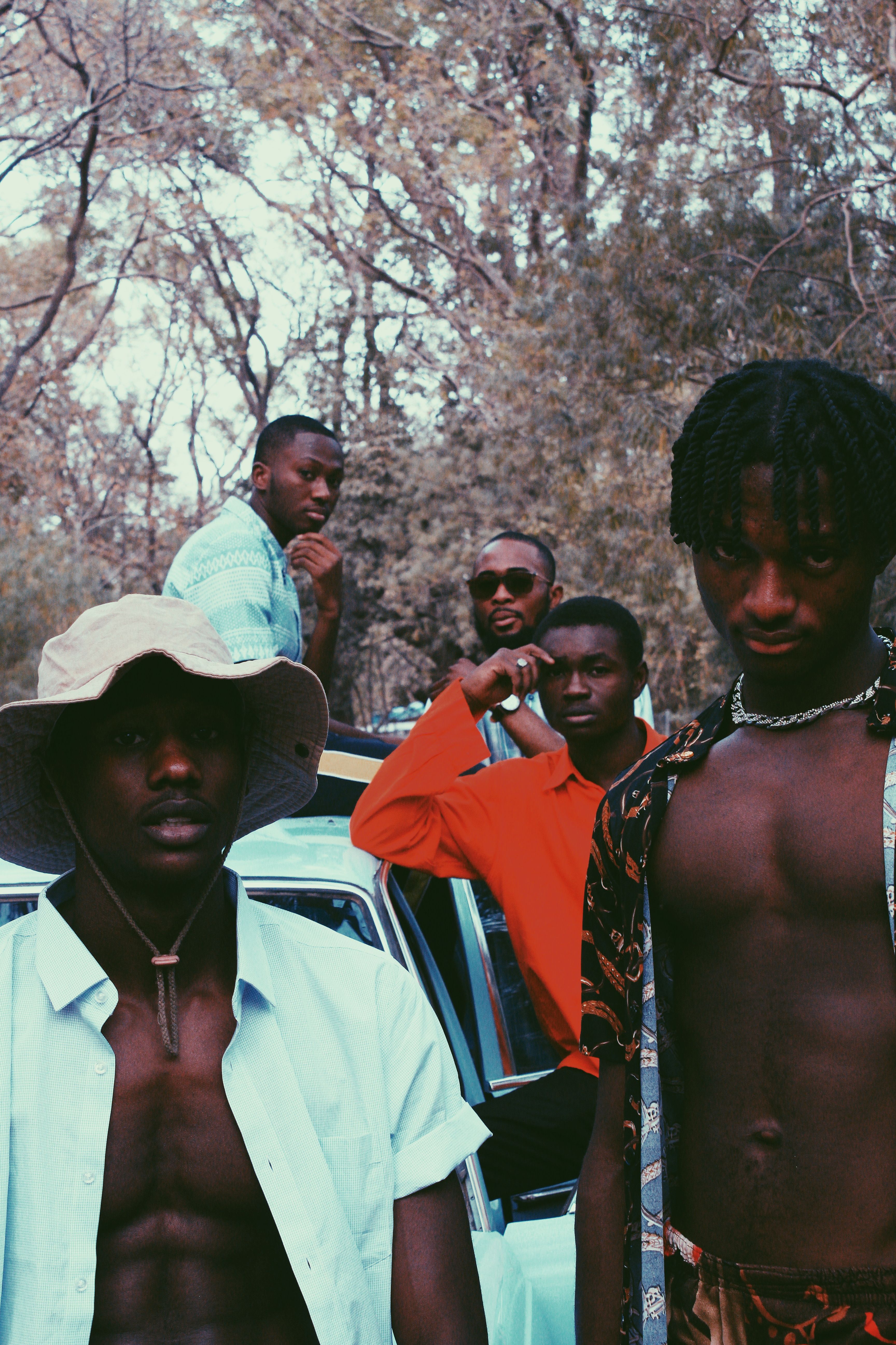 Confident black men in trendy clothes standing near old car and looking at camera against forest