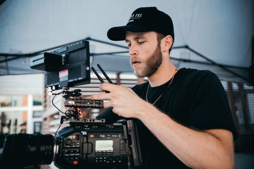 Free Bearded man in black cap adjusting professional camera equipment indoors. Stock Photo