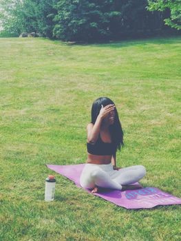 Young black woman practicing yoga outdoors on a sunny day sitting on a purple mat.