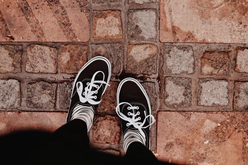 Free Looking down at black sneakers on a wet cobblestone path after rain. Stock Photo