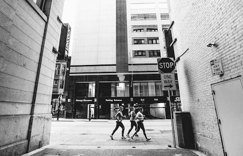 Grayscale Photo of People Walking on Sidewalk Near Builidngs