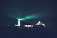 Green lighthouse in dark night on hill