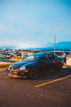 Amazing black automobile against modern cityscape with bright lights under blue cloudy sky in twilight