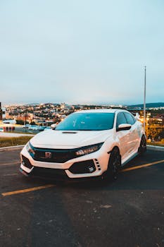 A modern white car parked outdoors in a city district, beautifully illuminated at twilight.