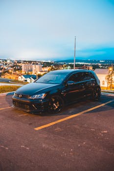 A modern black car parked in an urban setting at twilight with a cityscape background.