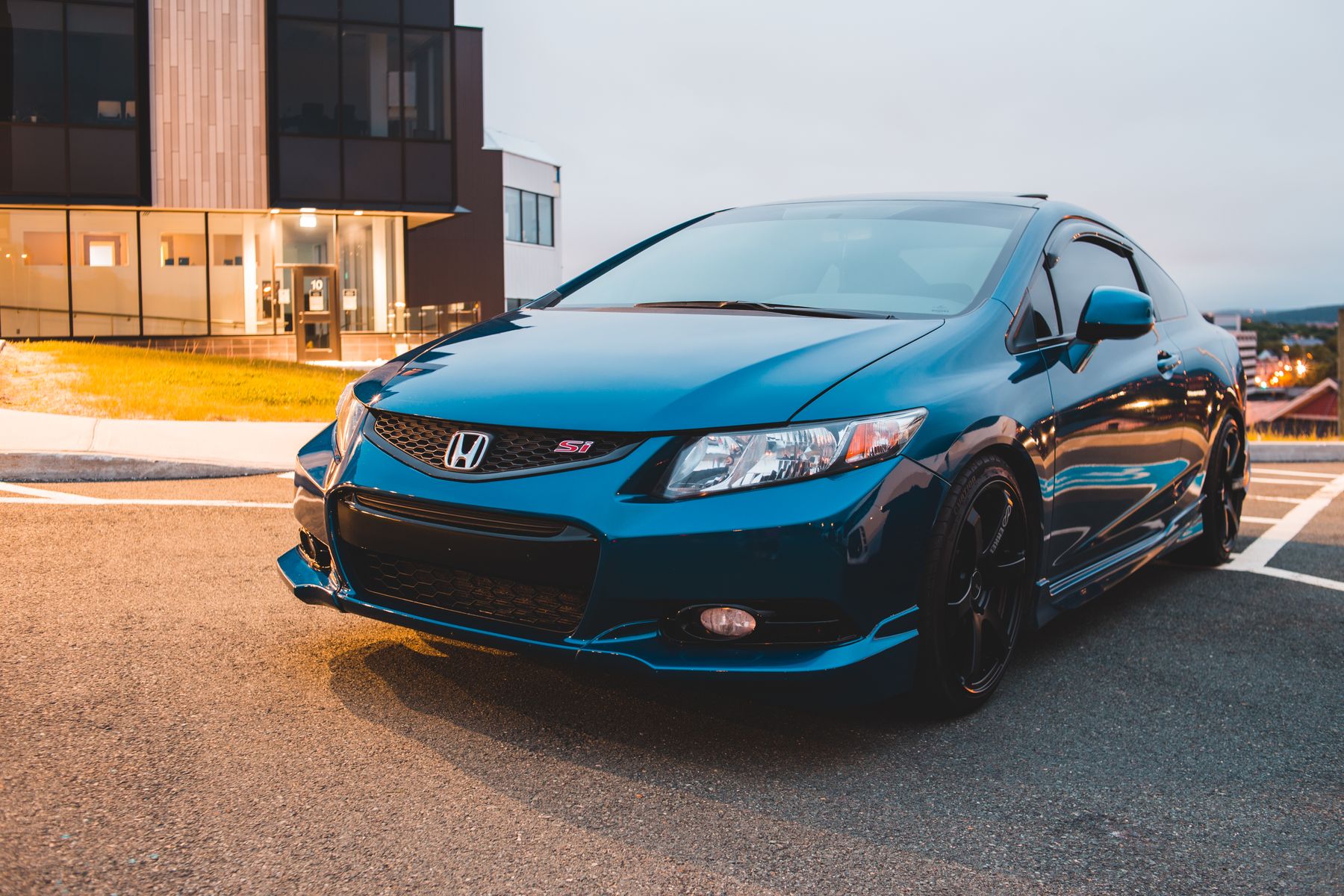 Blue performance car photographed beside a modern building at dusk