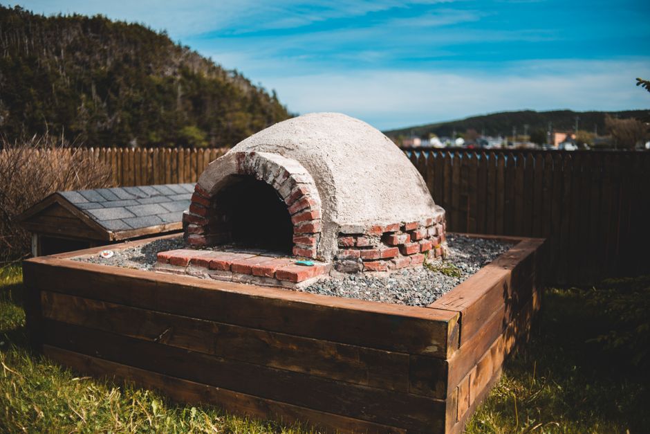 Photo by Erik Mclean on Pexels Aged outdoor pizza oven on wooden construction on grass behind mountains under blue cloudy sky