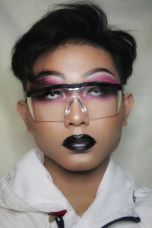 Young serious man with bright stylish unusual makeup on eyelids wearing glasses in studio