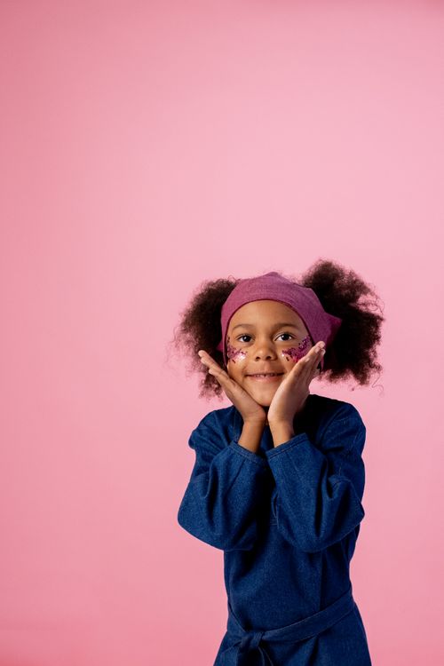 Free Adorable child posing indoors with face stickers and a playful expression against a pink background. Stock Photo