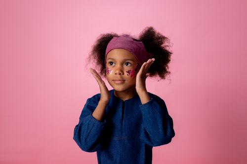 Free Cute child with glitter face stickers posing against a pink background in a studio. Stock Photo