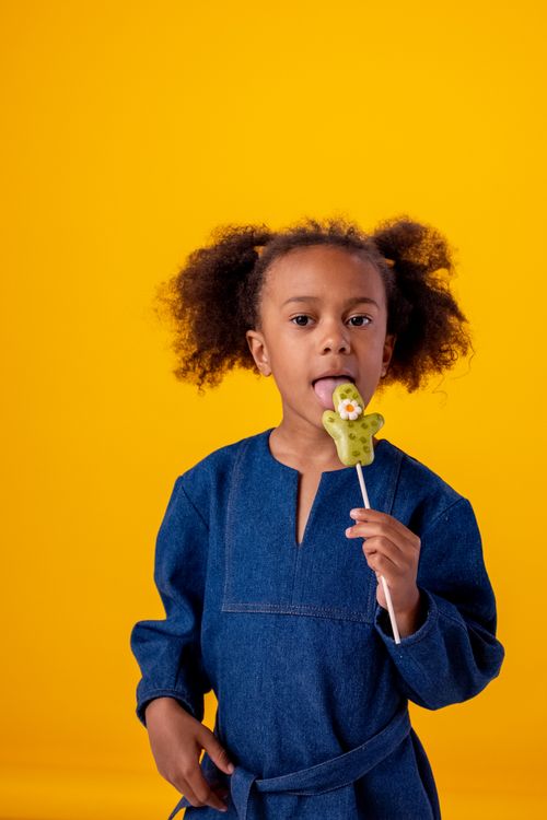 Free Adorable young girl licking a lollipop against a vibrant yellow background. Stock Photo