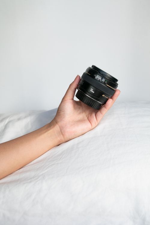 Free A hand holding a camera lens with a neutral soft backdrop, ideal for photography themes. Stock Photo