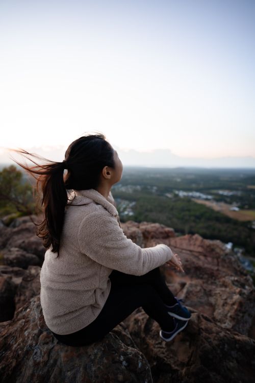 Free Woman sits on a rocky summit at Sunshine Coast, Australia, admiring a breathtaking vista. Stock Photo