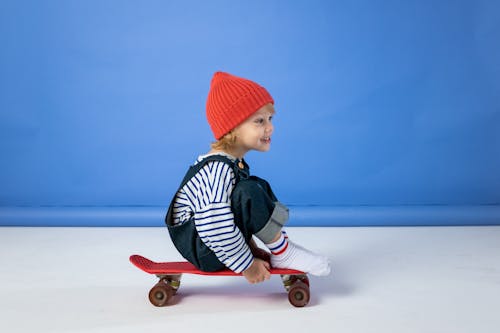 Child in Black and White Striped Long Sleeve Shirt and Red Knit Cap Sitting on Brown