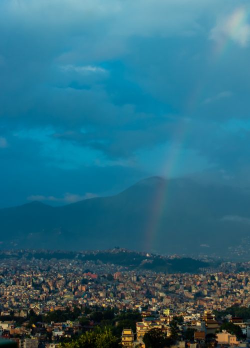 Free A captivating aerial shot of Kathmandu cityscape under a rainbow with majestic mountains in the background. Stock Photo